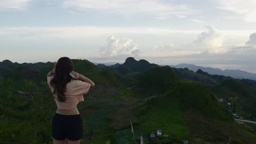 Cute woman in crop top and shorts adjusts hair as she stares off to sweeping tropical mountain view