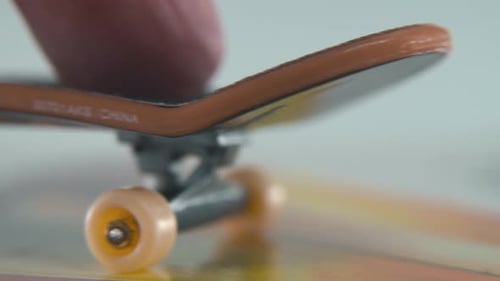 A hyper detailed shot of a mini skateboard, tiny white wheels, riding fingerboard from left to right