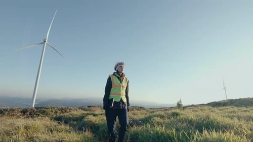 Female Engineer Walking with Tablet Through Wind Farm