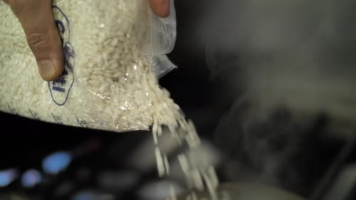 Pouring rice into pot with boiling water, close up