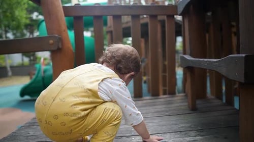 An adorable baby girl toddler playing and climbing on an outdoor playground set - slow motion