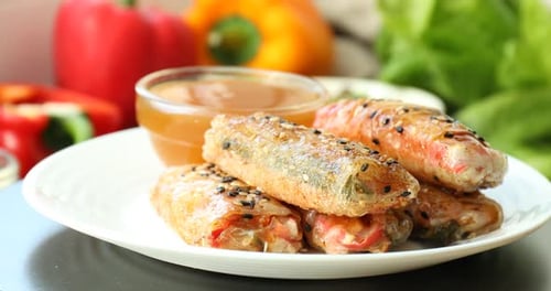 Plate with delicious fried spring rolls wrapped in rice paper and sauce turning against blurred