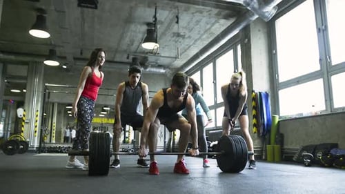 Young man's intense barbell workout in modern crossfit gym with friends