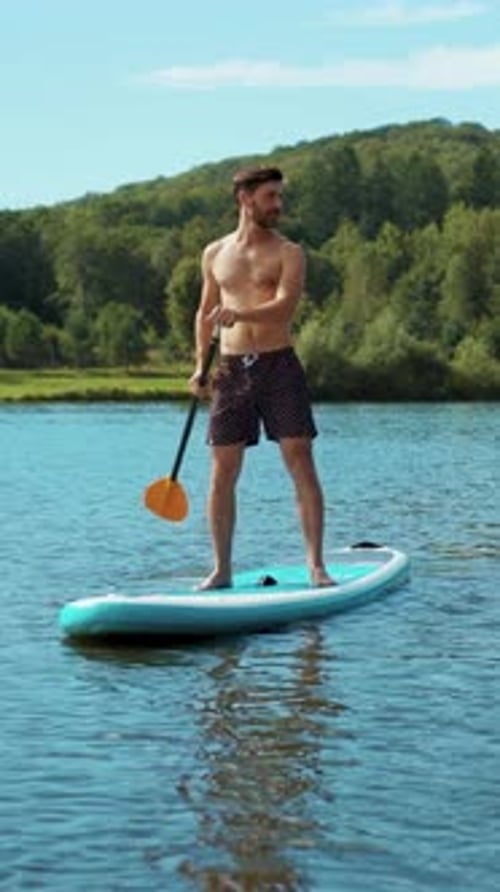 A Man is Paddle Boarding on a Calm and Serene Lake Enjoying Nature and Leisure Time Outdoors