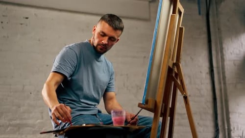 Young Artist in a Blue Tshirt in an Art Studio Working on Painting While Sitting