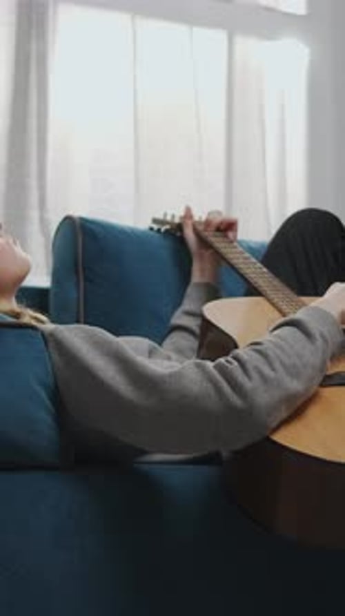 Woman Lies on Couch and Plays Guitar