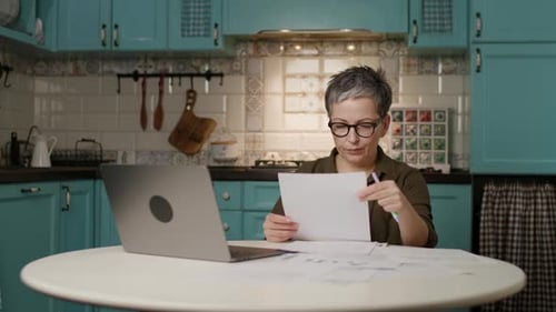 Woman Manages Paperwork While Using a Laptop at Home