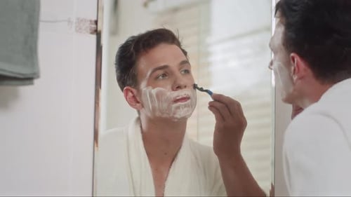 Homem usando navalha ao raspar a barba na frente do espelho