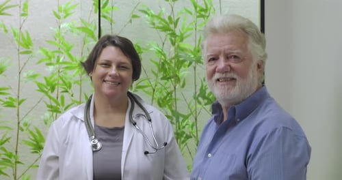 Female doctor and elderly male patient smiling together in clinic setting with green plants in