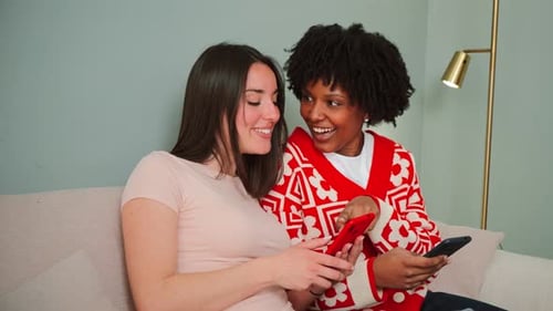 Two young women using smartphones indoors, smiling