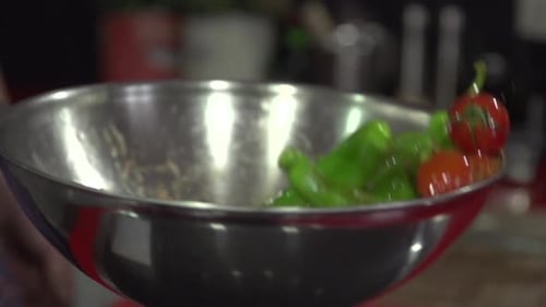 Slow motion shot of Green Long Chili Peppers and tomato being cooked in a silver pan with olive oil