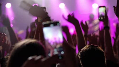 Konzertpublikum mit erhobenen Händen und Smartphones fängt die lebendige Atmosphäre einer Bühnenaufführung ein