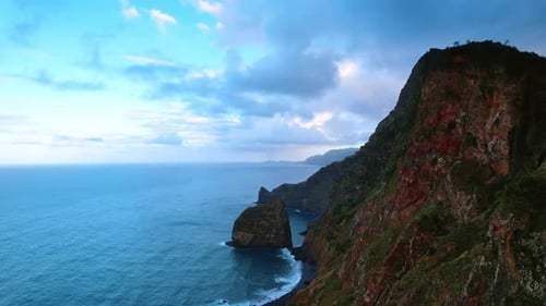 Picturesque high rocks with green lichens and mosses. Cloudy sky is above the blue waterscape.