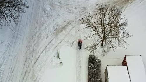 Person pushing snow blower and clearing pedestrian walkway on snowy winter day, aerial top view