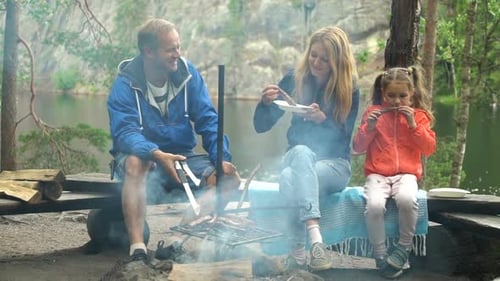 A Couple with a Child Grilling in the Forest on the Shore of the Lake
