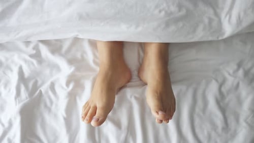 Woman Moving Feet on White Bed Sheets