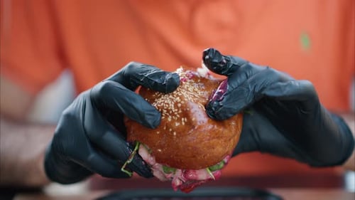 Man eating a burger with red sauce, black gum gloves, close up