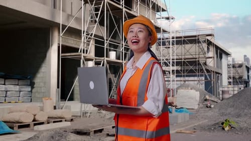 Seitenansicht einer asiatischen Ingenieurin, die auf einer Baustelle an einem Laptop arbeitet