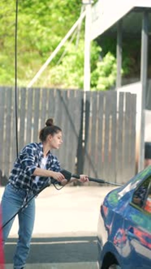Engaged at the Car Wash a Lovely Young Lady is Washing a Car Using a Highpressure Water Gun