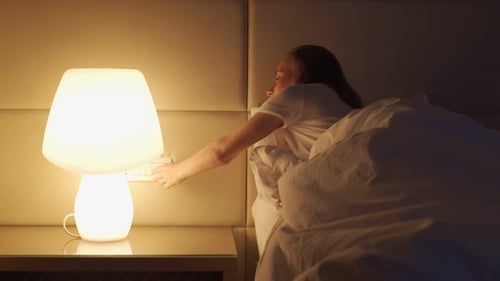 Mujer se mete en la cama apagando la lámpara brillante en la mesita de noche