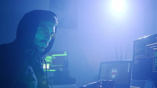 Dans une pièce sombre remplie d'écrans d'ordinateur lumineux, un mystérieux hacker opère en secret