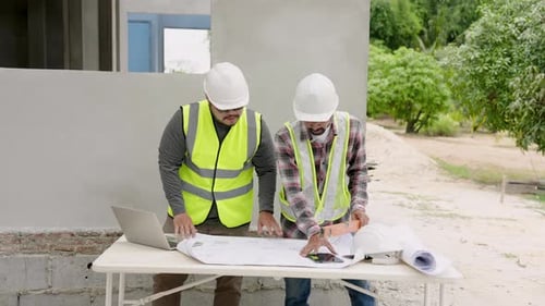 Indian construction architect and foreman Checking construction plans from blueprints and in laptop