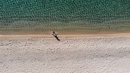 Woman walking in shallow water along a beach filmed with a drone.