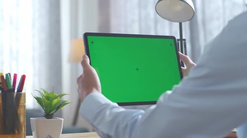 Close up of man's hands holding a mock up green screen tablet on a desk