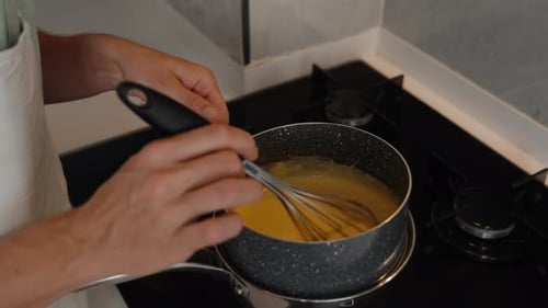 La femme remue la purée avec un fouet dans la casserole de la cuisinière à gaz et la caméra zoome lentement.