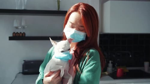 Red-Haired Asian Woman Holding Small Dog Both Wearing Blue Masks