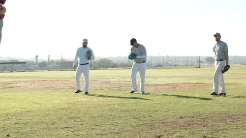 Pitching male baseball teammates practicing catch drill in outfield, with baseball and gloves