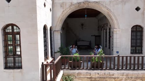 Women Chatting on Balcony with Stone Architecture