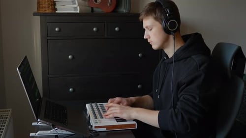 Young man creating music in his home studio, focusing on sound engineering using a laptop and MIDI c
