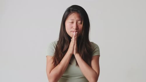 Young woman hold hands folded in prayer, making wish isolated over white background in studio
