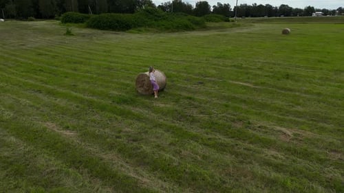 Elevated View Woman Seated on a Hay Bale in a Picturesque Grassy Field