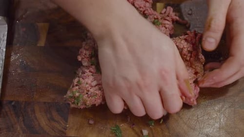 Mashing ground beef on wooden cut board. Close up on hands. Cooking Rigatoni con polpettes (meatbal