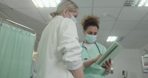 Doctor and Nurse looking at Medical Results on Digital tablet in Hospital wearing Face mask.