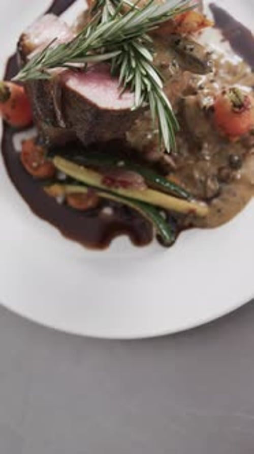 Upper view of prepared and decorated meal on white plate on in kitchen, slow motion, vertical