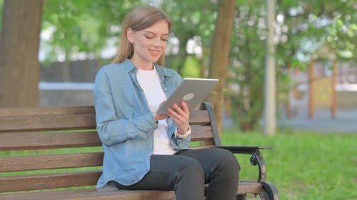 Woman Uses Tablet on Park Bench in Daytime