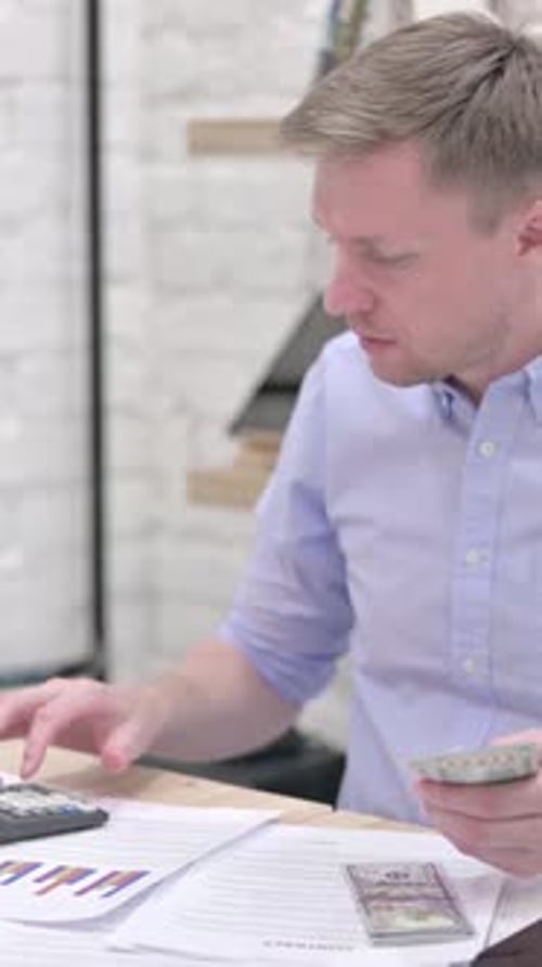 Man Counts Money and Uses Calculator at Desk