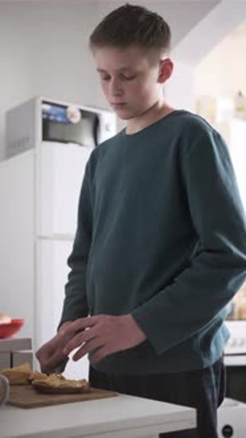 Adolescent préparant le petit-déjeuner en étalant du beurre sur du pain dans la cuisine, atmosphère décontractée