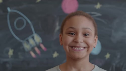 Child Smiles in Front of Rocket Drawing on Chalkboard