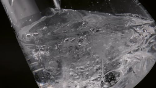 Pouring Fresh Water in Glass with Ice Cubes Close Up. Crystal Liquid
