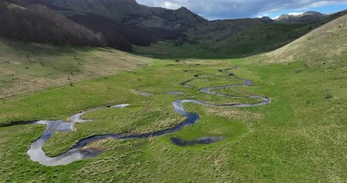 Flug über einen gewundenen Gebirgsbach mit klarem Wasser an einem sonnigen Frühlingstag. Der Bach fließt durch
