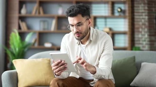 Young Adult Browsing Tablet on Couch at Home