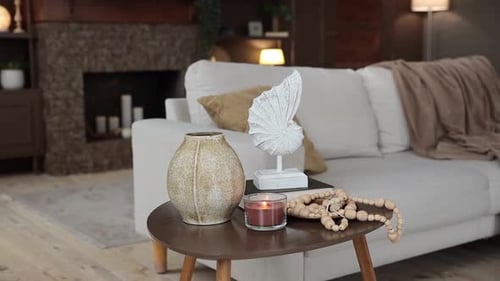 A Coffee Table with a Stylish Decor and a Burning Candle on a Blurred Background of a Sofa with