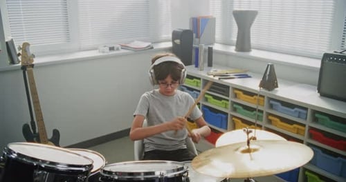 Primary School Boy Wearing Headphones Practicing Drums in Modern Music Class