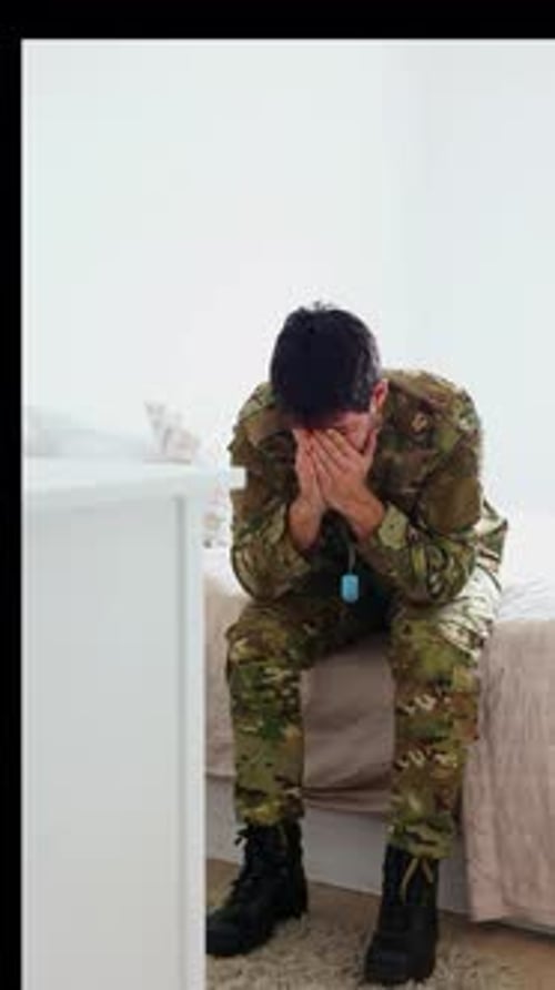 vertical Depressed soldier sitting on bed, suffering from post-traumatic stress disorder