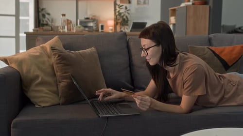Woman using laptop computer holding credit card at home