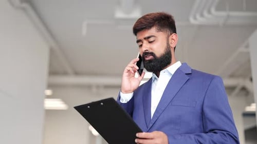 Man Talks on Phone Holding Clipboard in Office